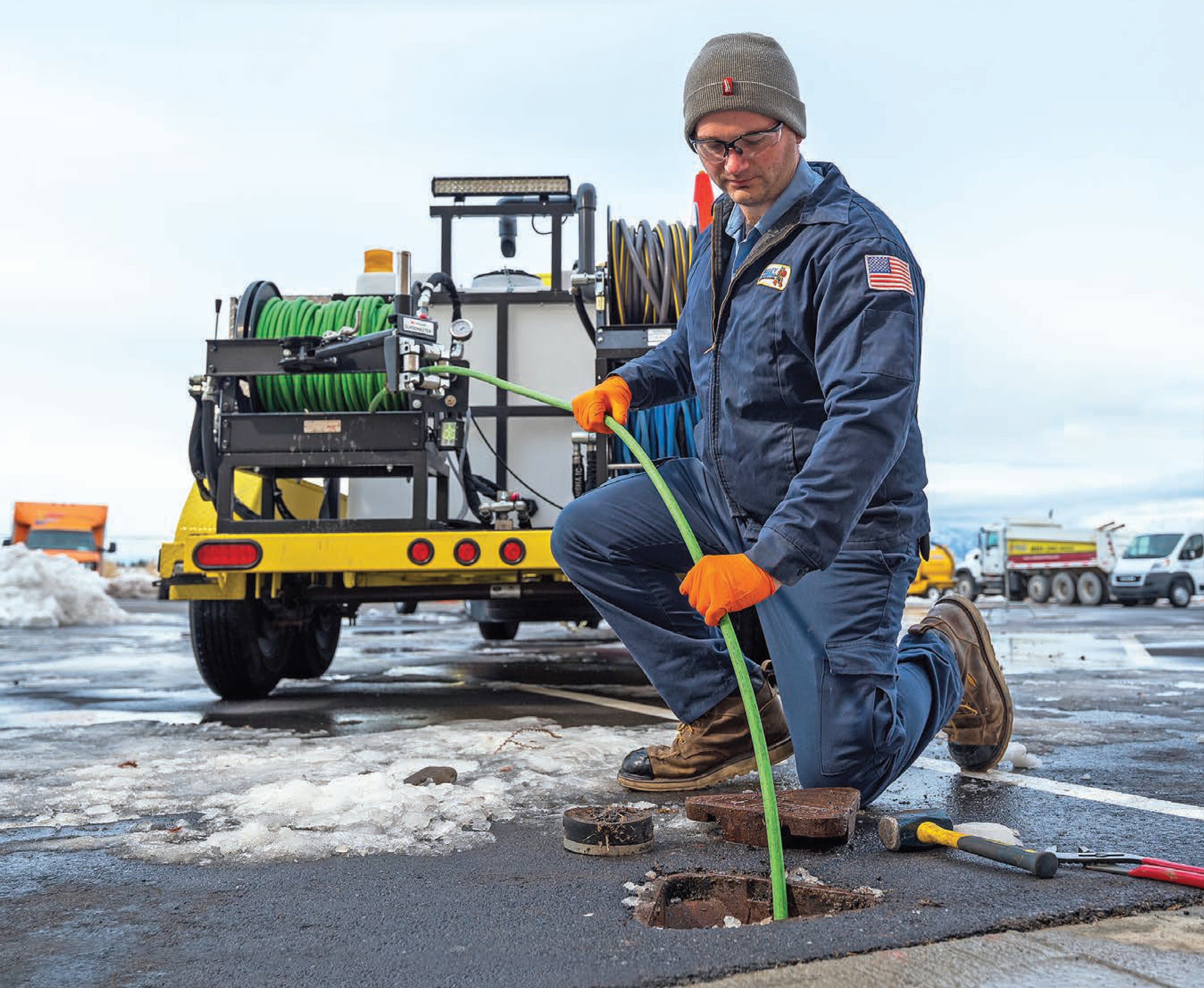 Technician feeding a jetting hose into a drain beside sewer jetting equipment